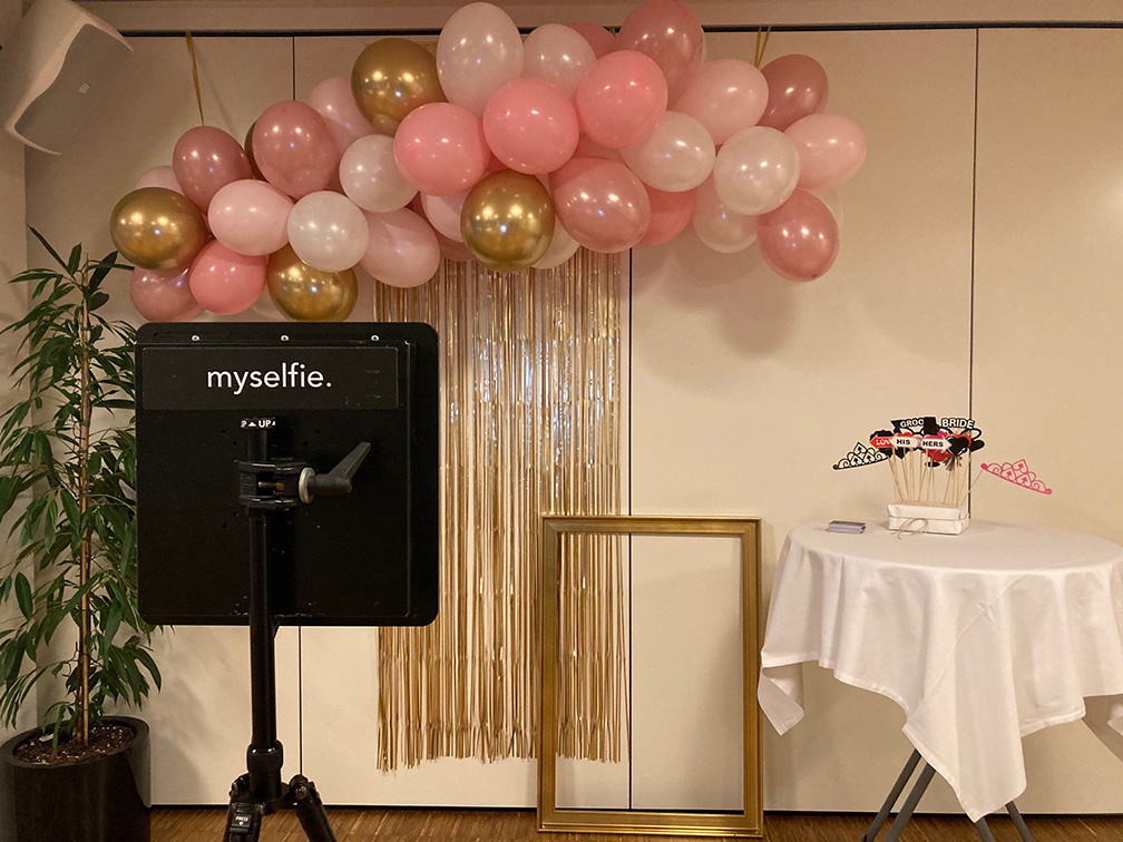 Fotohjørne med balloner i rosa og guld, myselfie-station og sjove rekvisitter – klar til festlige minder.
