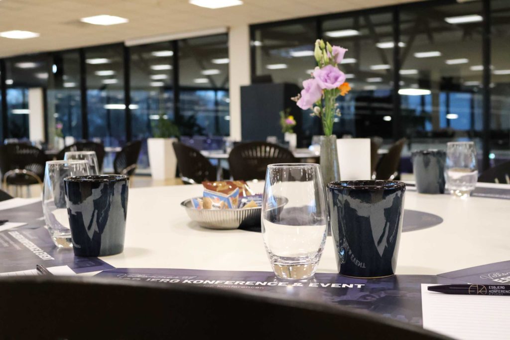 Claus Sørensen Lounge dækket op til møde med kaffekopper, vandglas, notesblokke og blomster
