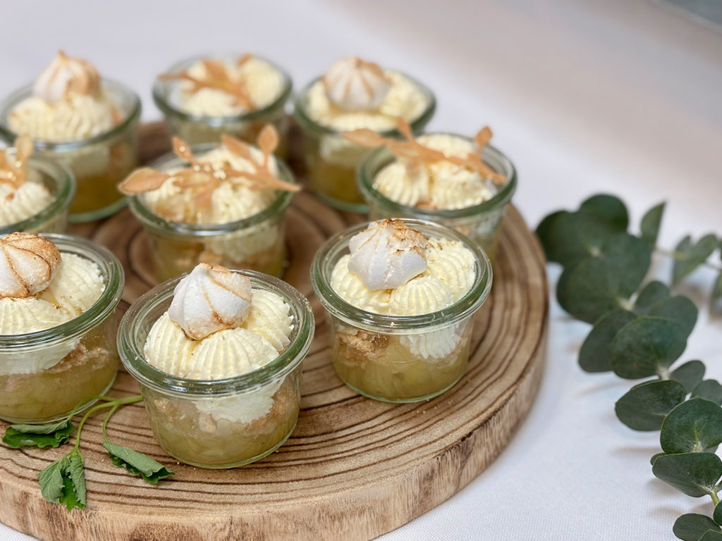 Små glas med klassisk æblekage toppet med flødeskum, bagt marengs og pynt – smukt anrettet på træfad af husets egen konditor.