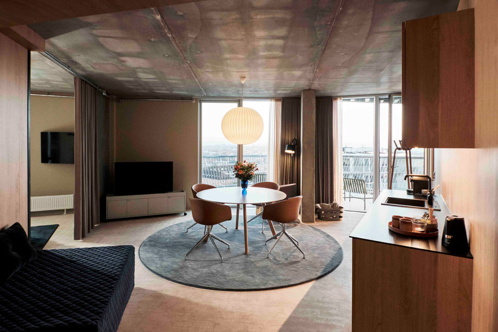 Moderne hotelværelse på A Place To Hotel Esbjerg med spisebord, sofa, køkkenområde og store vinduer med udsigt over byen.