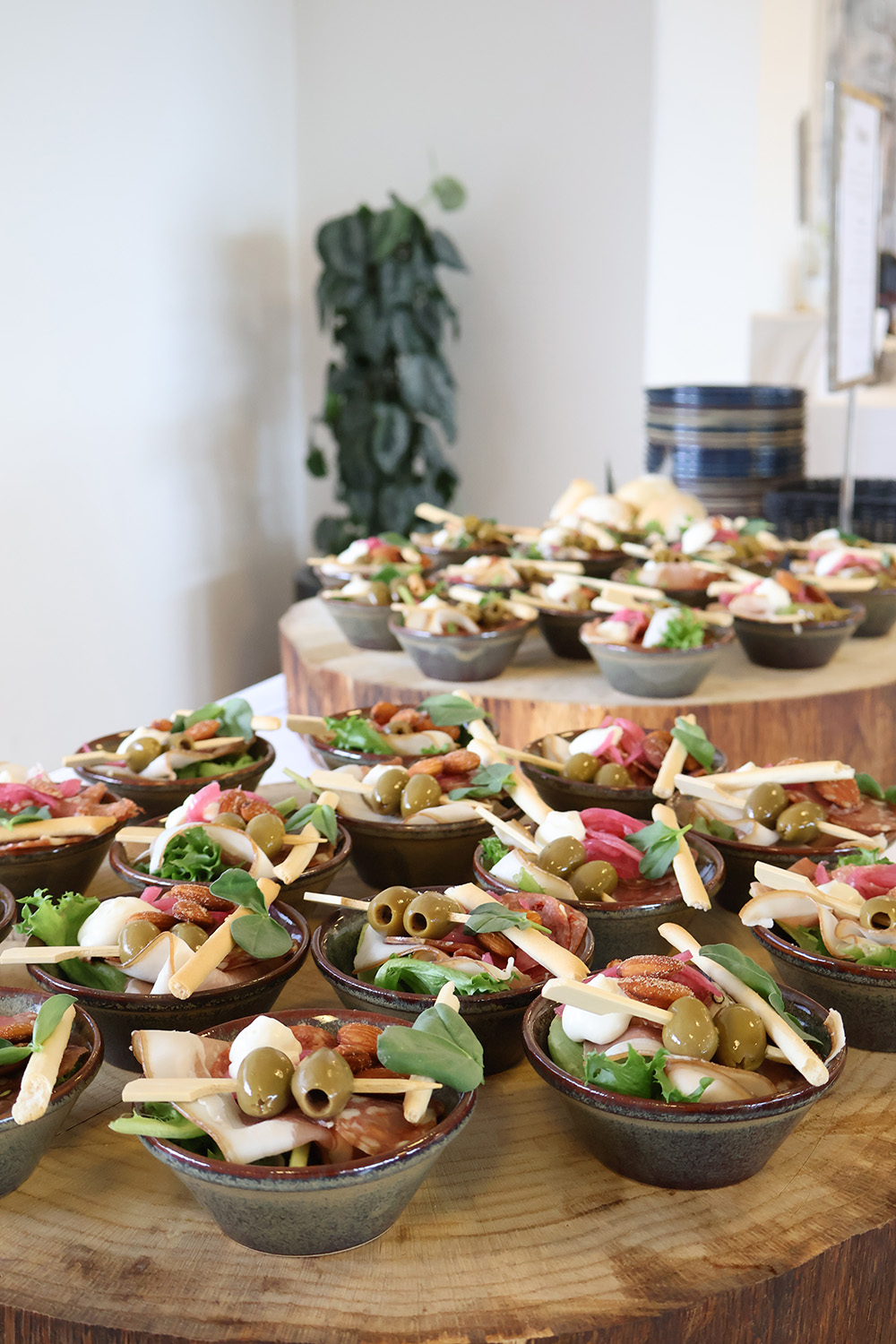Små portionsanretninger med oliven, ost, serranoskinke, chorizo og grønt stilfuldt opstillet på træfade ved buffet.