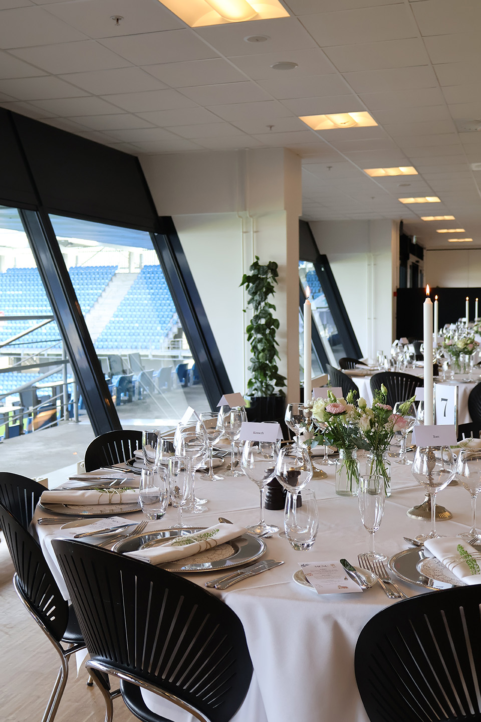 Rundt festbord dækket med glas, sølvservice og blomster med udsigt til tribunen på Blue Water Arena.
