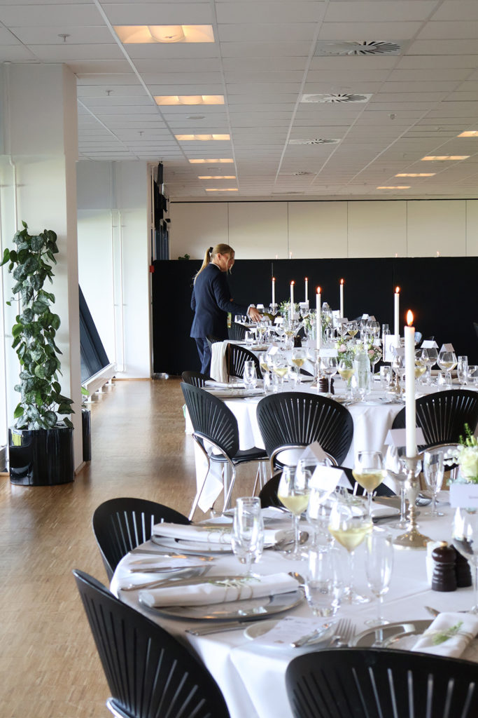 Personale gør klar til festligt dækkede borde med vin og stearinlys til bryllup hos Esbjerg Konference & Event i Carlsberg Loungen.