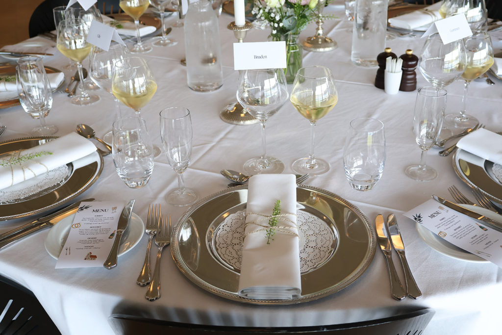 Elegant borddækning med sølvservice, hvide servietter og vin klar til bryllupsmiddag hos Esbjerg Konference & Event.