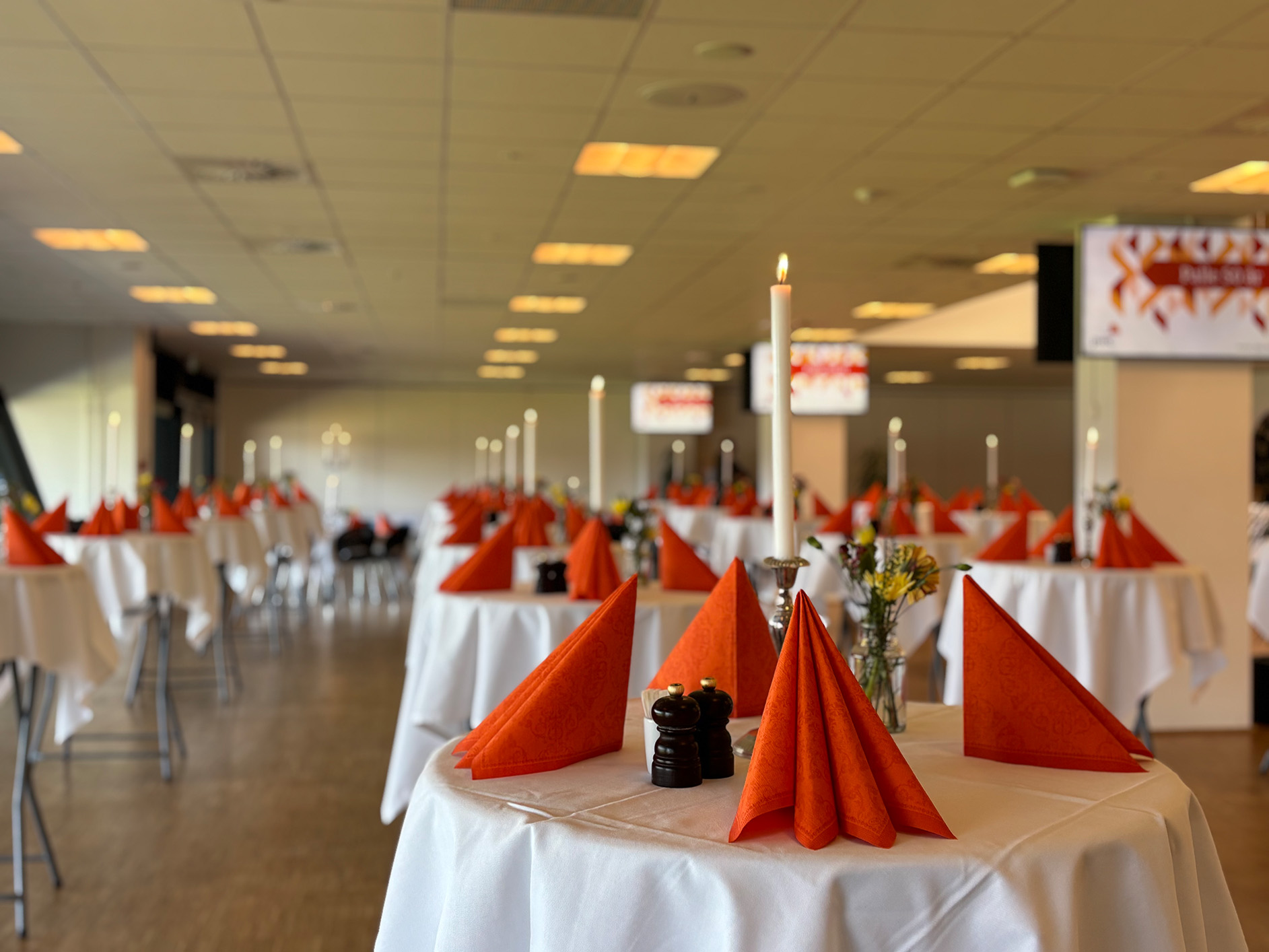 Festlokale dækket op med hvide duge, orange servietter og levende lys klar til reception i loungen hos Esbjerg Konference & Event.