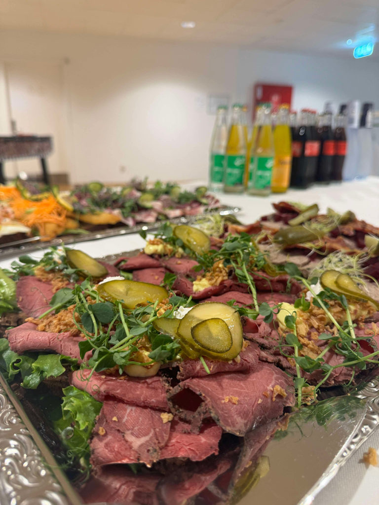 Serveringsfade med smørrebrød toppet med roastbeef, pickles og grønt pynt klar til frokostbuffet.