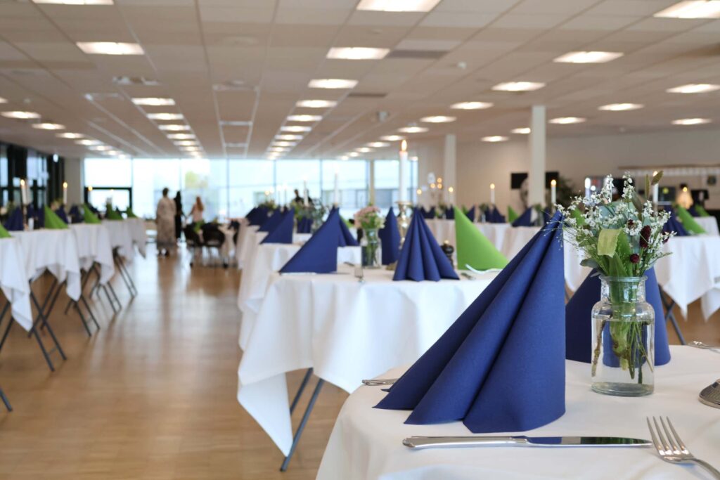 Receptionslokale i Esbjerg med ståborde dækker op med blå og grønne servietter, levende lys, blomster og bestik