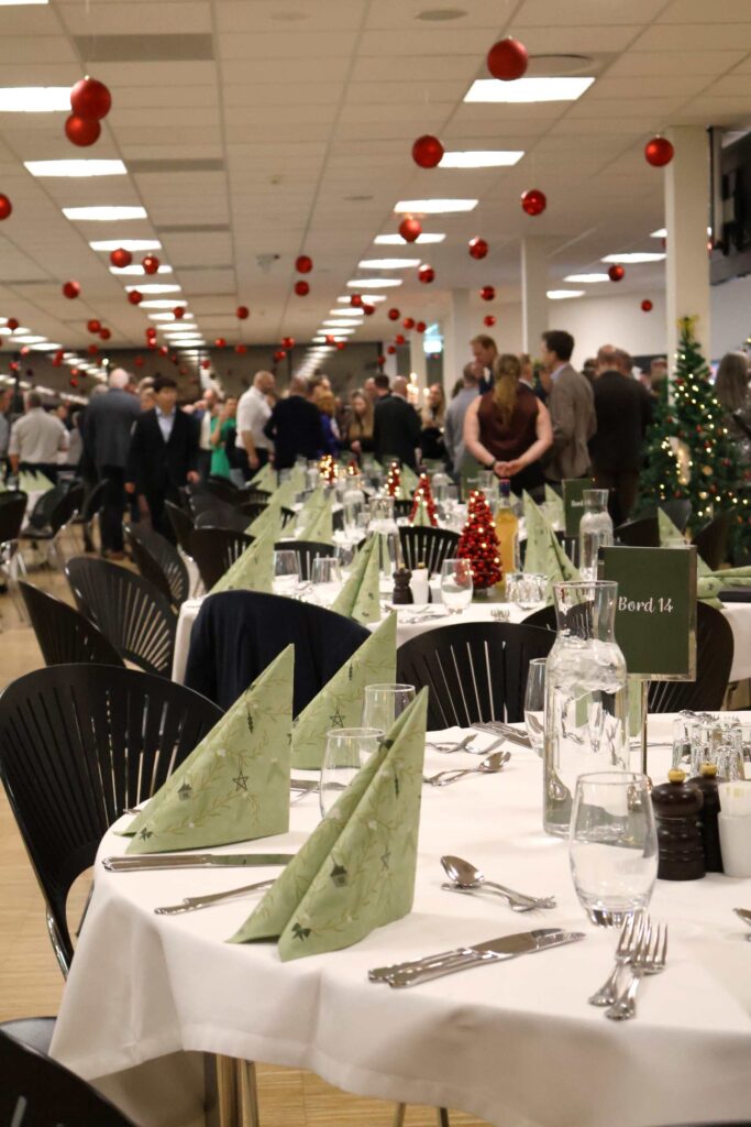 Runde borde opdækket til julefrokost med gæster i baggrunden og røde julekugler i loftet