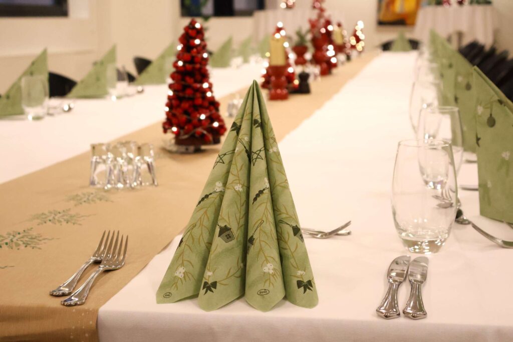 Juleopdækning til julefrokost med grøn serviet, snapsglas, røde juletræer med lys i, bestik og glas
