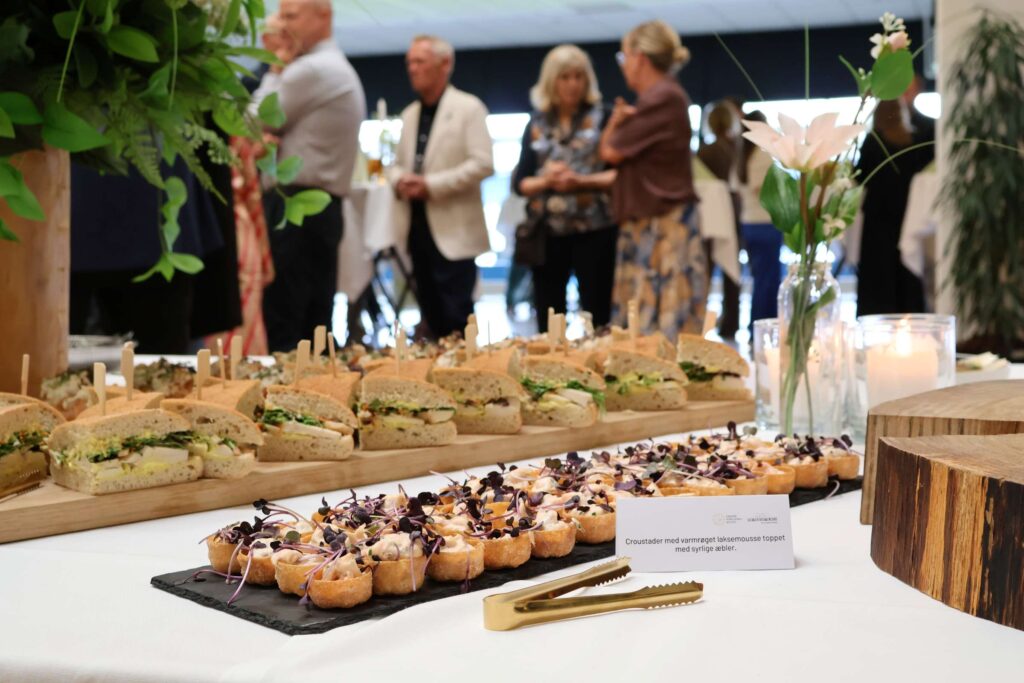 Receptionsbuffet med 10 små forskellige retter på pynter bord med levende lys og blomster med gæster i baggrunden