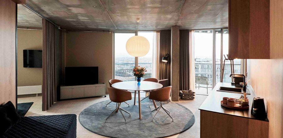 Moderne hotelværelse på A Place To Hotel Esbjerg med spisebord, sofa, køkkenområde og store vinduer med udsigt over byen.