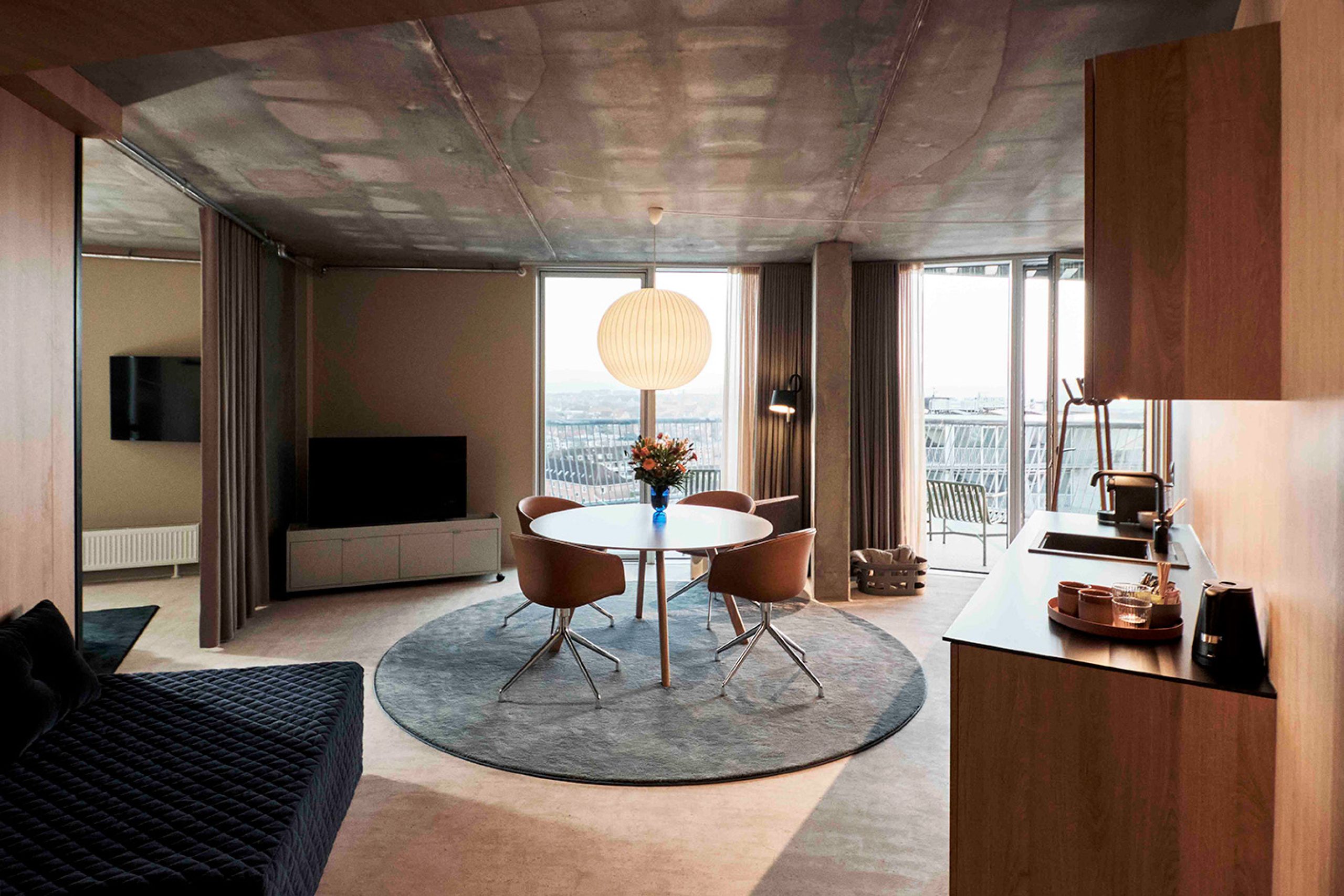 Moderne hotelværelse på A Place To Hotel Esbjerg med spisebord, sofa, køkkenområde og store vinduer med udsigt over byen.