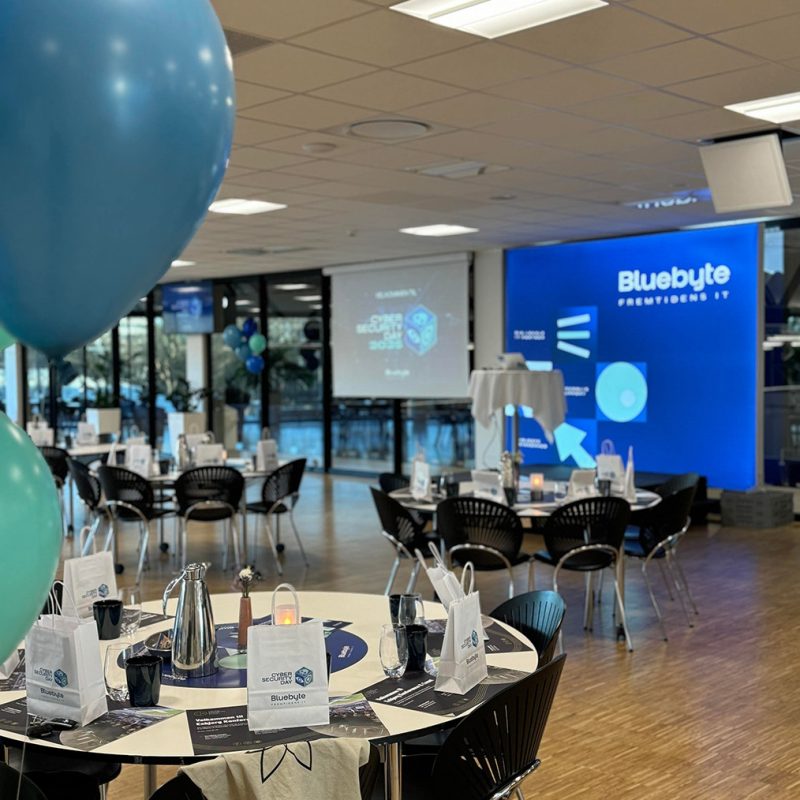 Mødeopdækning med balloner og runde borde i moderne lokale, klar til firmaarrangement med Bluebyte-tema.