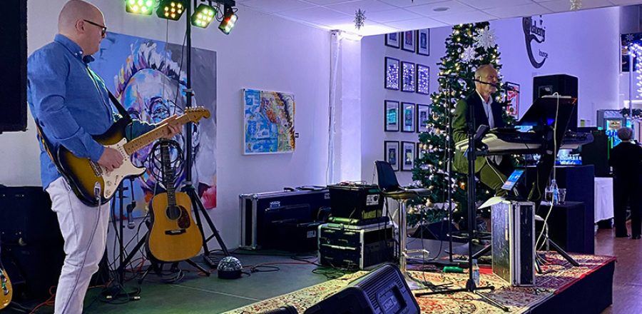 Band spiller livemusik på scenen til Den Store Julefrokost, omgivet af julepynt og festlig belysning.”