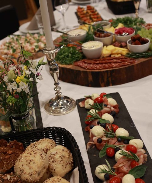 Smukt dækket bord med tapas, friskbagt brød, charcuteri, mozzarella og tomater – omgivet af blomster og stearinlys til en festlig middag