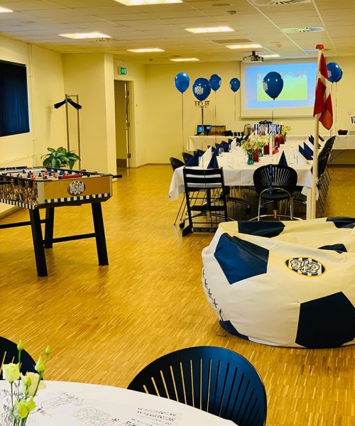 Festligt lokale pyntet til børnefødselsdag med fodboldtema, EfB-balloner, fodboldbord og en stor sækkestol formet som en bold.