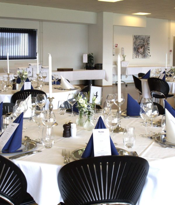 Opdækket borde i Carlsberg Lounge 1 med runde borde, hvide duge og blå servietter. Klar til en festlig fejring i lokale på Blue Water Arena.