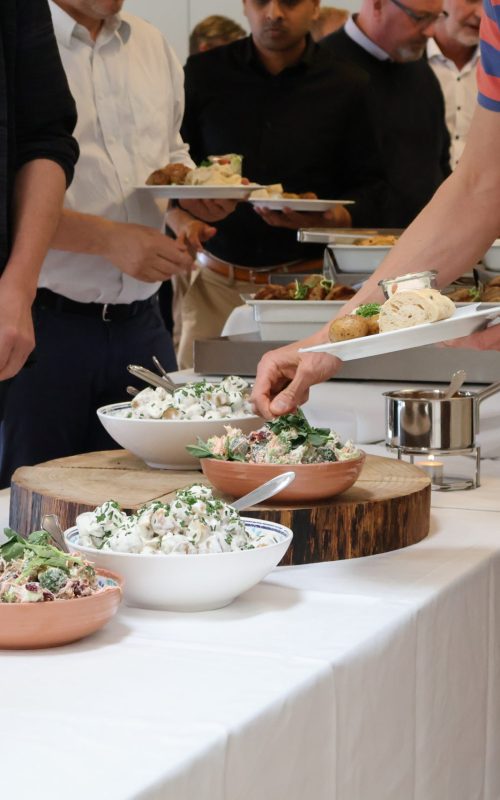 Gæster tager mad fra buffet med salater, kød og brød under frokostarrangement hos Esbjerg Konference & Event.