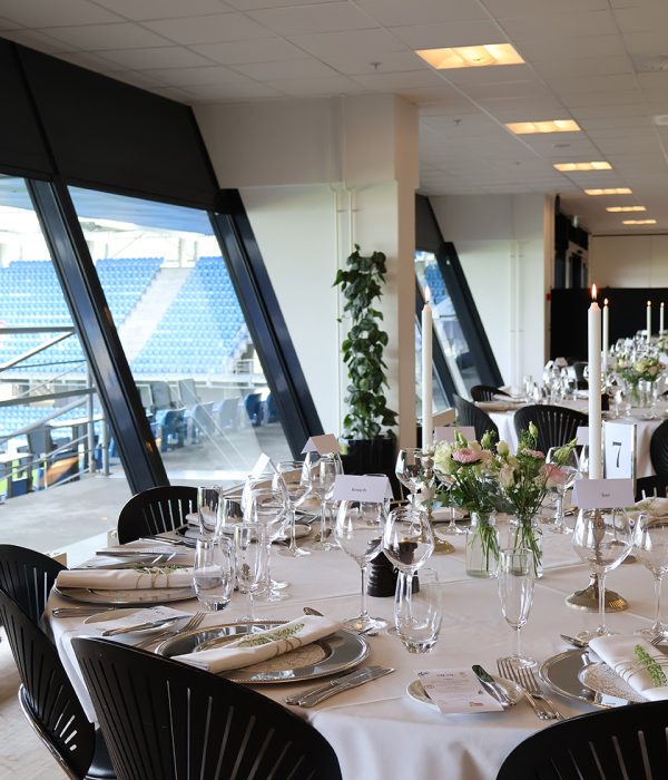 Rundt festbord dækket med glas, sølvservice og blomster med udsigt til tribunen på Blue Water Arena.