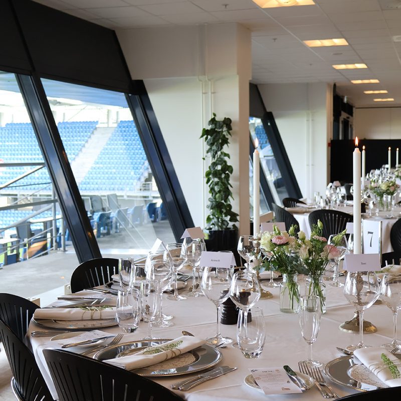 Rundt festbord dækket med glas, sølvservice og blomster med udsigt til tribunen på Blue Water Arena.