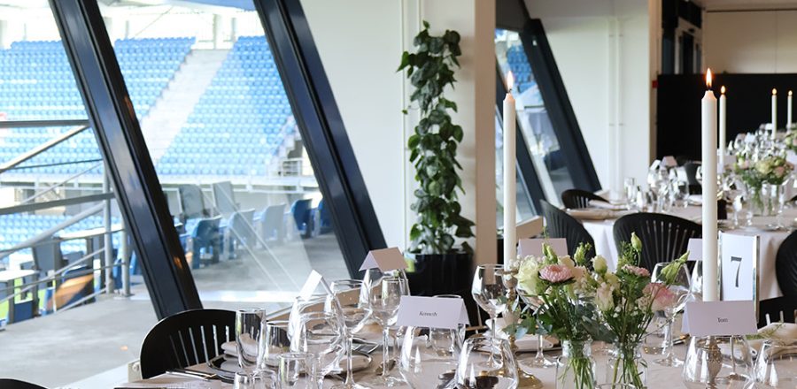 Rundt festbord dækket med glas, sølvservice og blomster med udsigt til tribunen på Blue Water Arena.