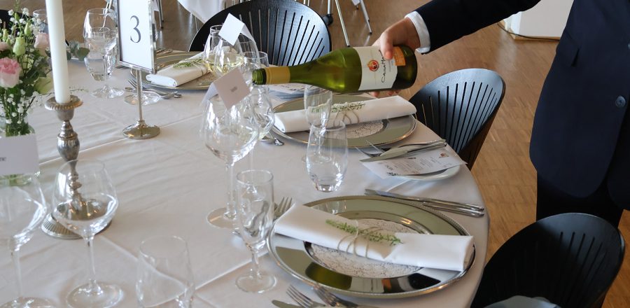 Servicemedejler hælder vin ved elegant opdækket bord med sølvservice og blomster til bryllupsarrangement hos Esbjerg Konference & Event