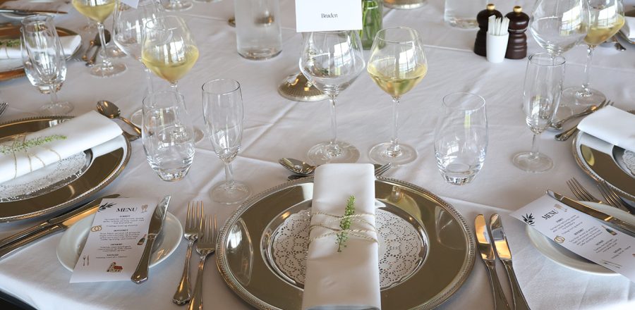 Elegant borddækning med sølvservice, hvide servietter og vin klar til bryllupsmiddag hos Esbjerg Konference & Event.