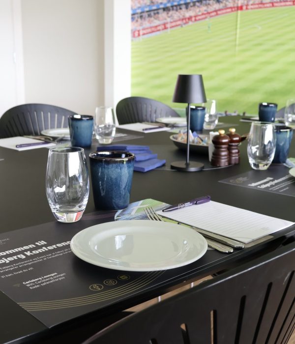Opdækning til møde i Skybox på Blue Water Arena med glas og kaffekopper, notesblok og tallerkenener.