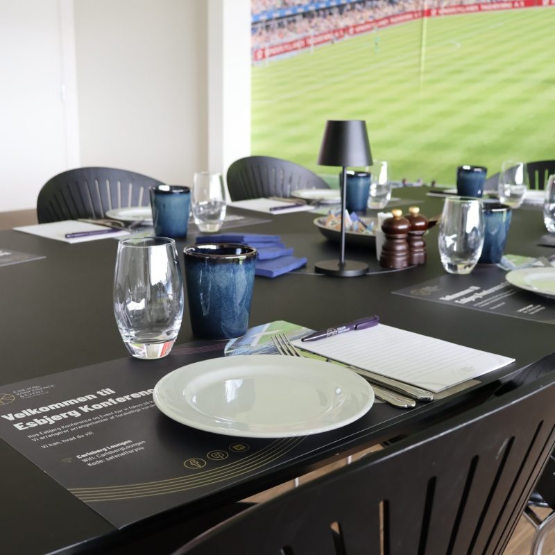 Opdækning til møde i Skybox på Blue Water Arena med glas og kaffekopper, notesblok og tallerkenener.