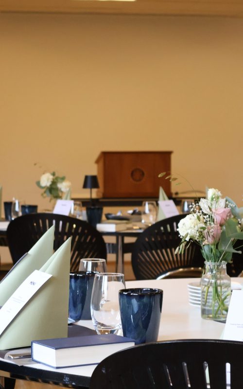 Rundt bord dækket med blomster, menukort og servietter klar til møde eller selskab i Skylounge hos Esbjerg Konference & Event.