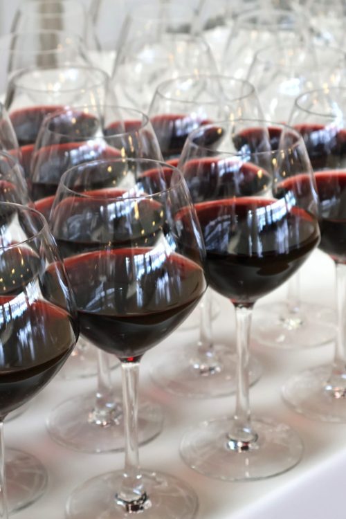 Rækker af rødvinsglas gjort klar til servering på hvid dug – klar til at byde gæsterne velkommen til en elegant middag i stemningsfulde omgivelser.