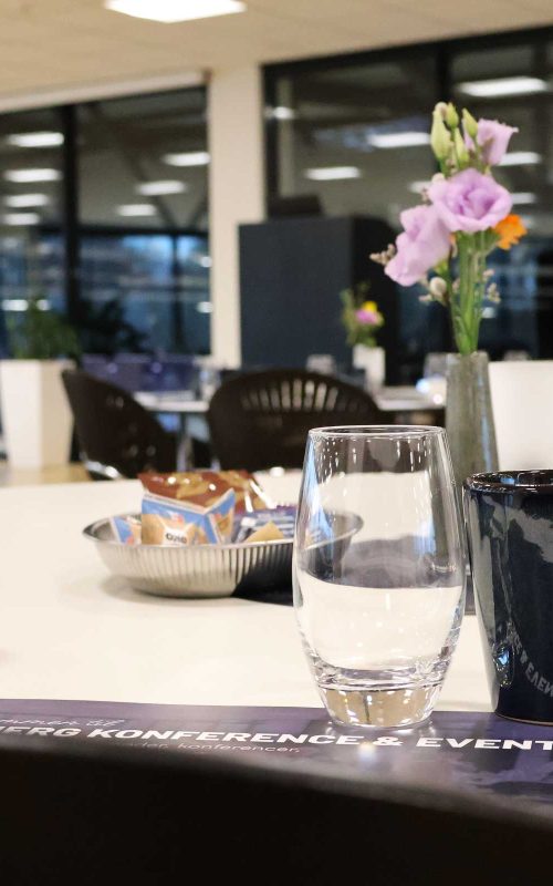 Claus Sørensen Lounge dækket op til møde med kaffekopper, vandglas, notesblokke og blomster