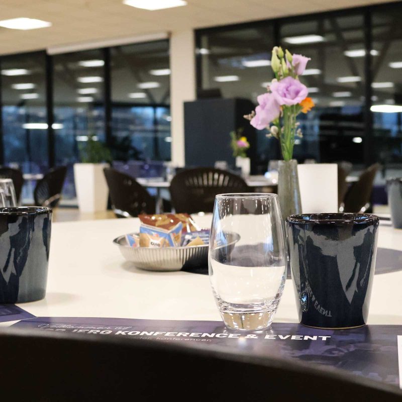 Claus Sørensen Lounge dækket op til møde med kaffekopper, vandglas, notesblokke og blomster