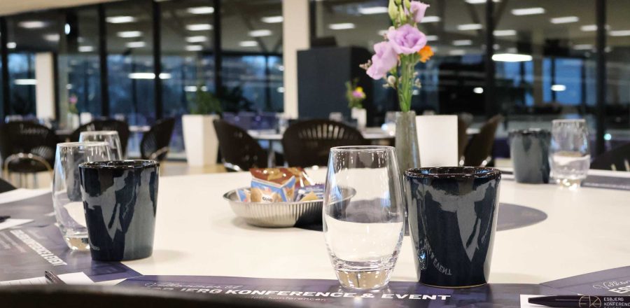 Claus Sørensen Lounge dækket op til møde med kaffekopper, vandglas, notesblokke og blomster