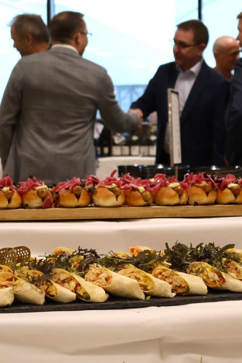Gæster hilser bagved buffet med gourmet hotdogs og andre små retter til reception