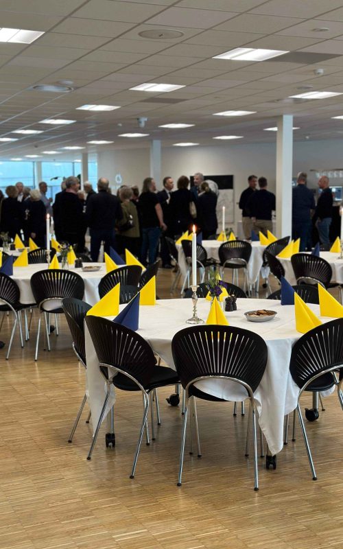 Selskabelig sammenkomst i EKEs festlokale med gæster samlet for snak og opdækkede runde borde.