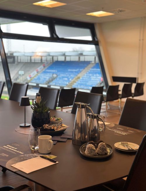Mødebord i skybox med kaffe, kage og udsigt til tribunen på Blue Water Arena.