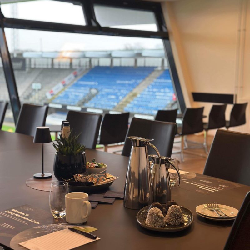 Mødebord i skybox med kaffe, kage og udsigt til tribunen på Blue Water Arena.