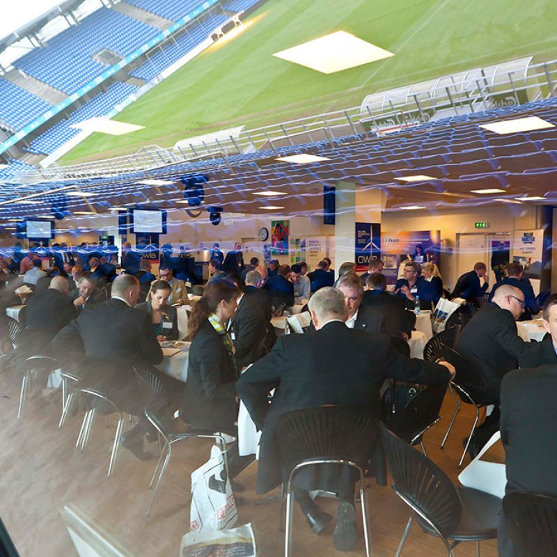Erhvervsnetværkssammenkomst i loungeområdet med udsigt til stadion – et rum fyldt med samtaler, relationer og forretning.