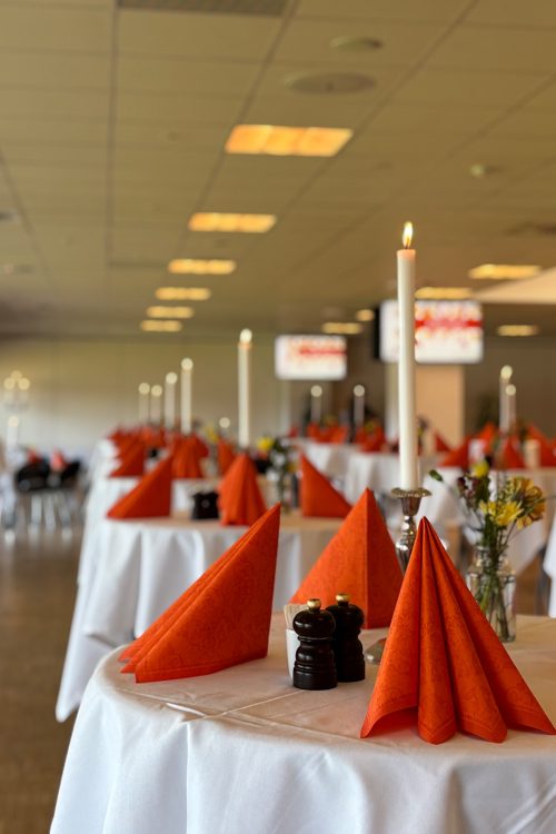 Festlokale dækket op med hvide duge, orange servietter og levende lys klar til reception i loungen hos Esbjerg Konference & Event.