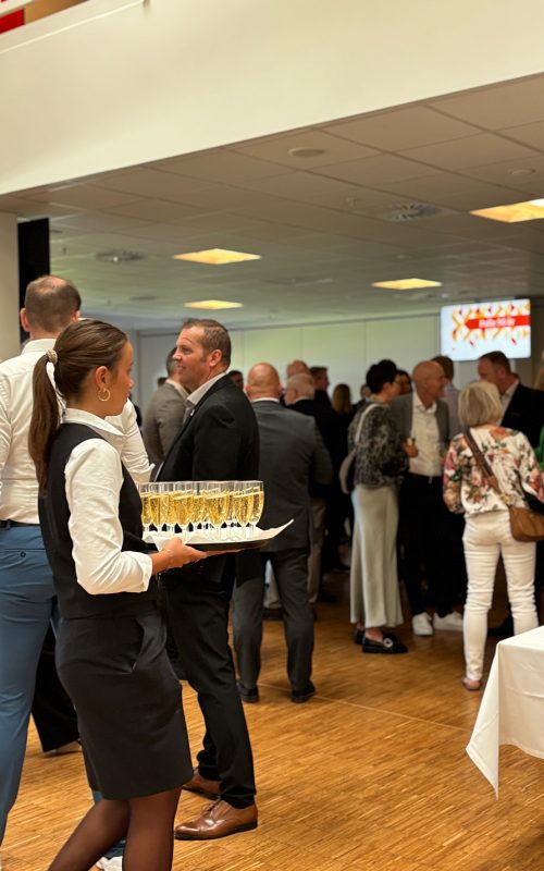 Servitrice serverer velkomstbobler for gæster ved et festligt arrangement i loungen på Blue Water Arena.