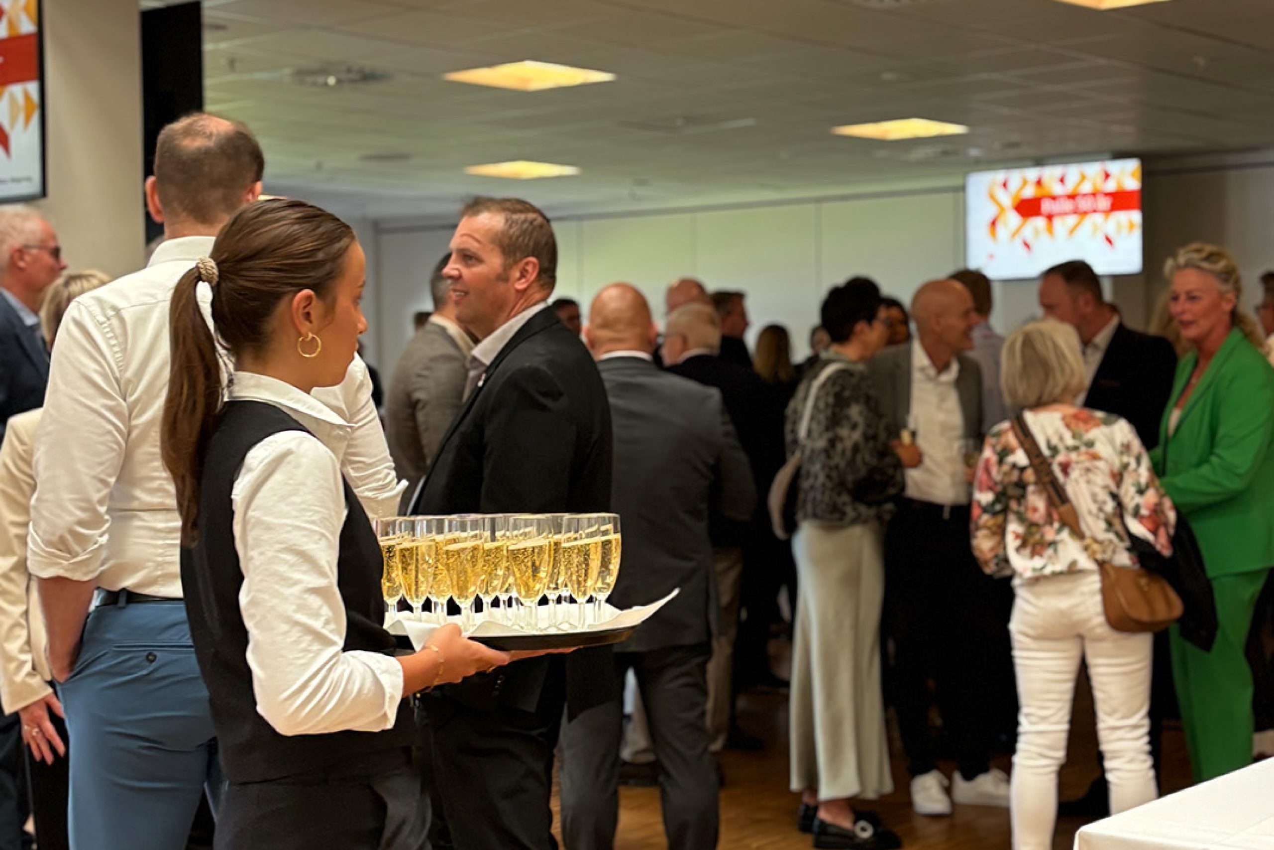 Servitrice serverer velkomstbobler for gæster ved et festligt arrangement i loungen på Blue Water Arena.